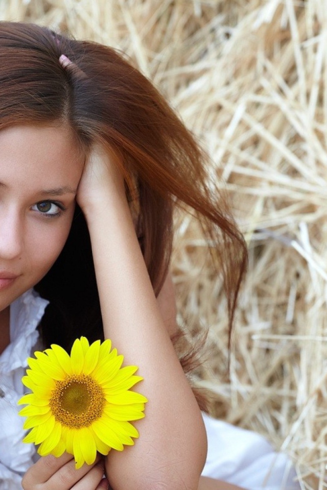 Девушка с желтым цветком сидит на сене