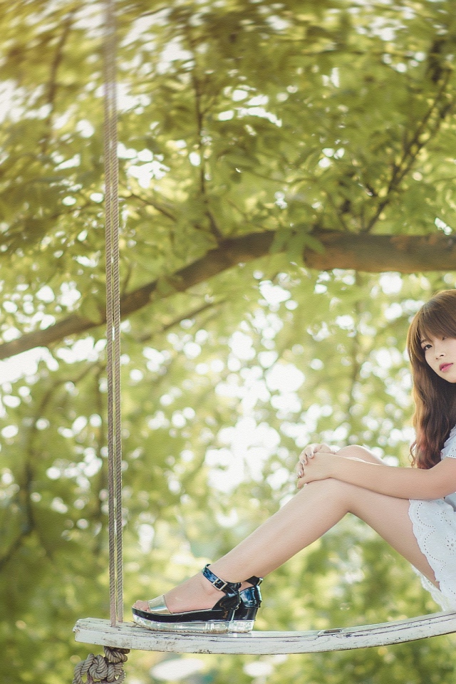 Японская девушка в белом платье сидит на качелях