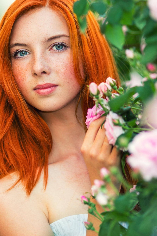 Рыжая девушка прячется за цветущими ветками