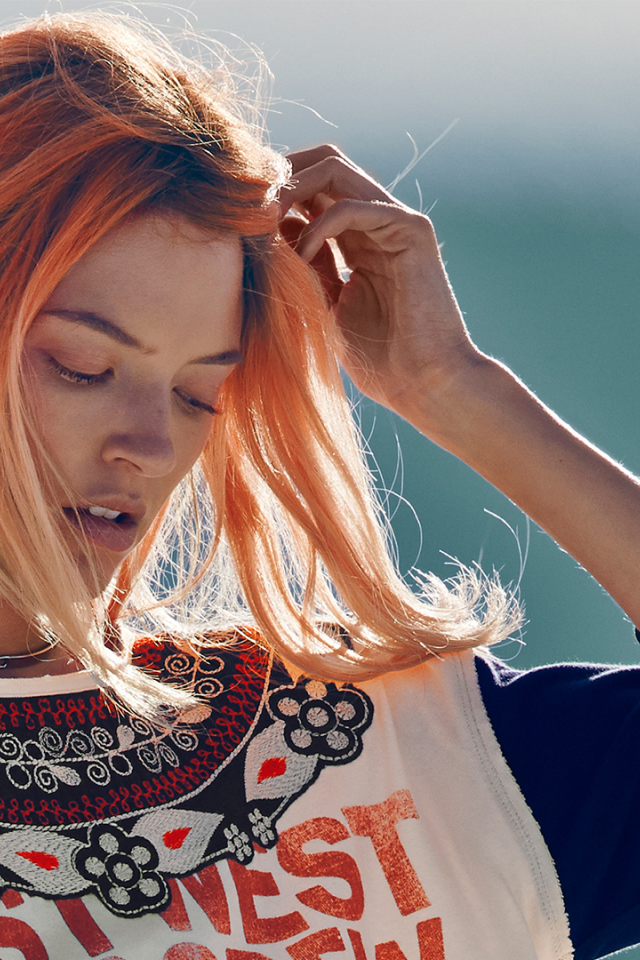 Рыжая девушка на ветру поправляет волосы