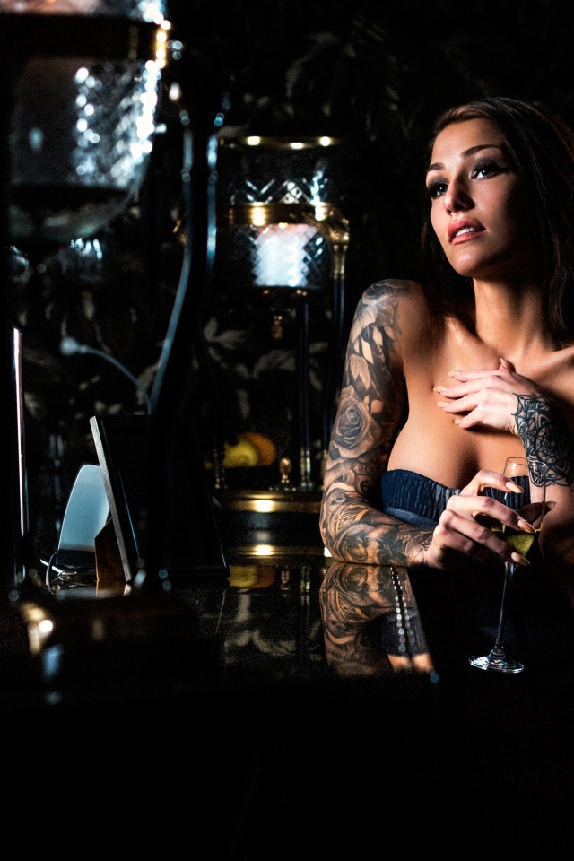 Татуированная девушка пьет вино в баре