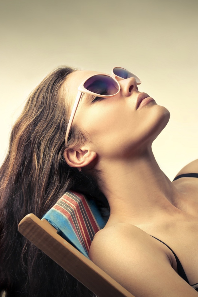 Девушка в очках загорает в шезлонге