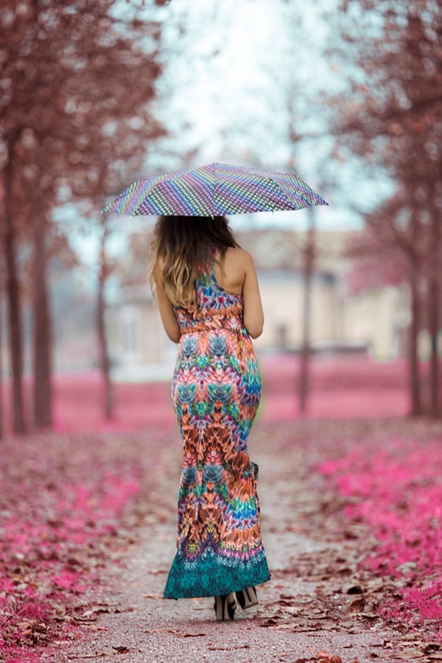 The girl under an umbrella in a beautiful dress goes through the alley