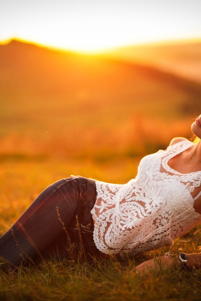 Модель в джинсах позирует на закате солнца