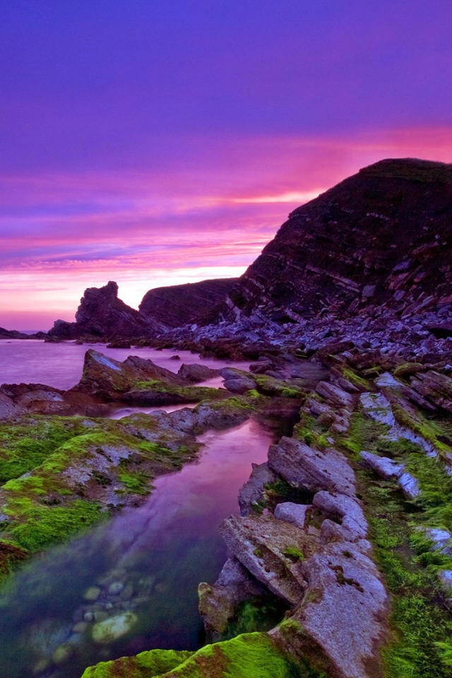 Голые скалы у берега на фоне сиреневого заката