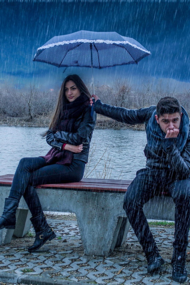 Парень держит над девушкой зонт во время дождя