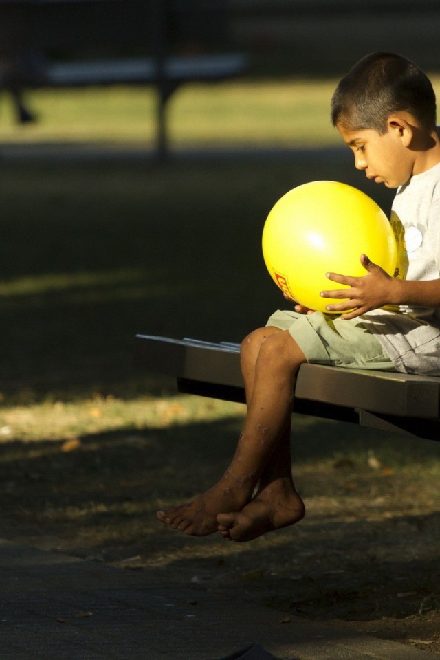 Мальчик сидит на скамье с шариком в руках