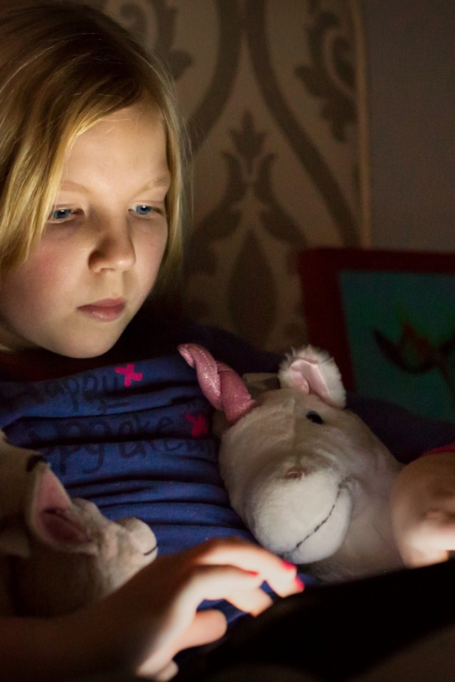 Девочка играет с планшетом лежа в кровати