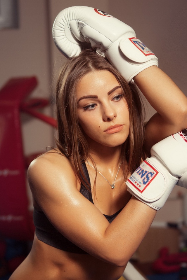 Девушка в белых перчатках отдыхает у канатов ринга