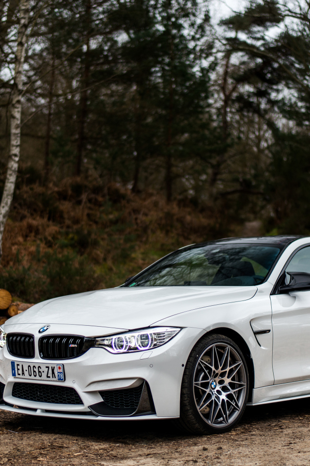 Белый стильный автомобиль BMW M4 на фоне деревьев