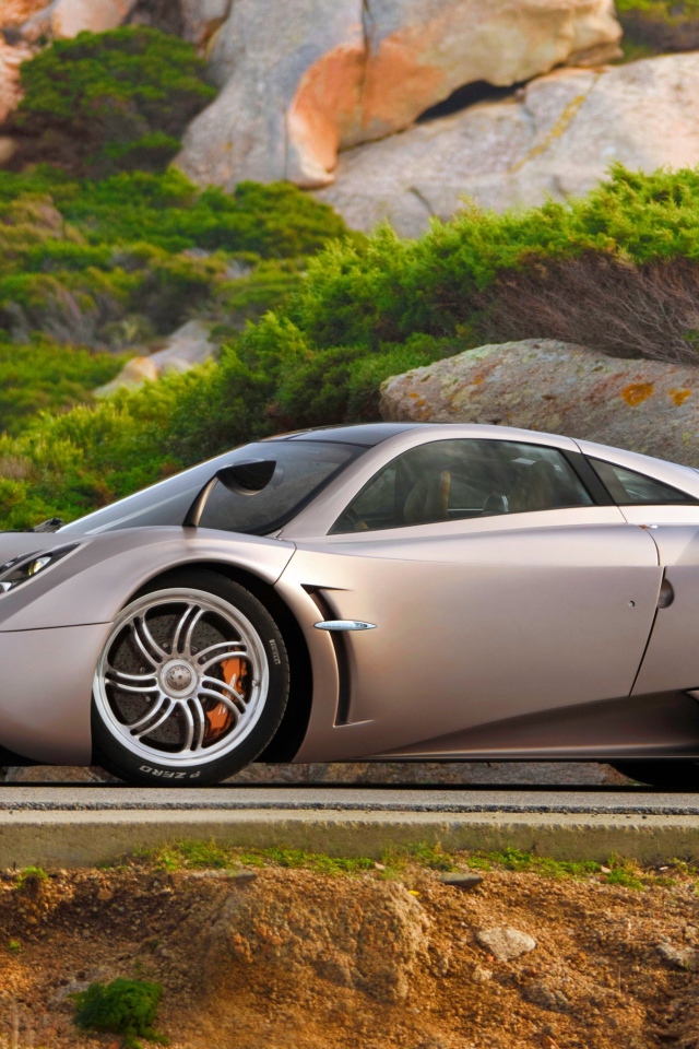 Серебристый быстрый автомобиль  Pagani Huayra на трассе у скалы