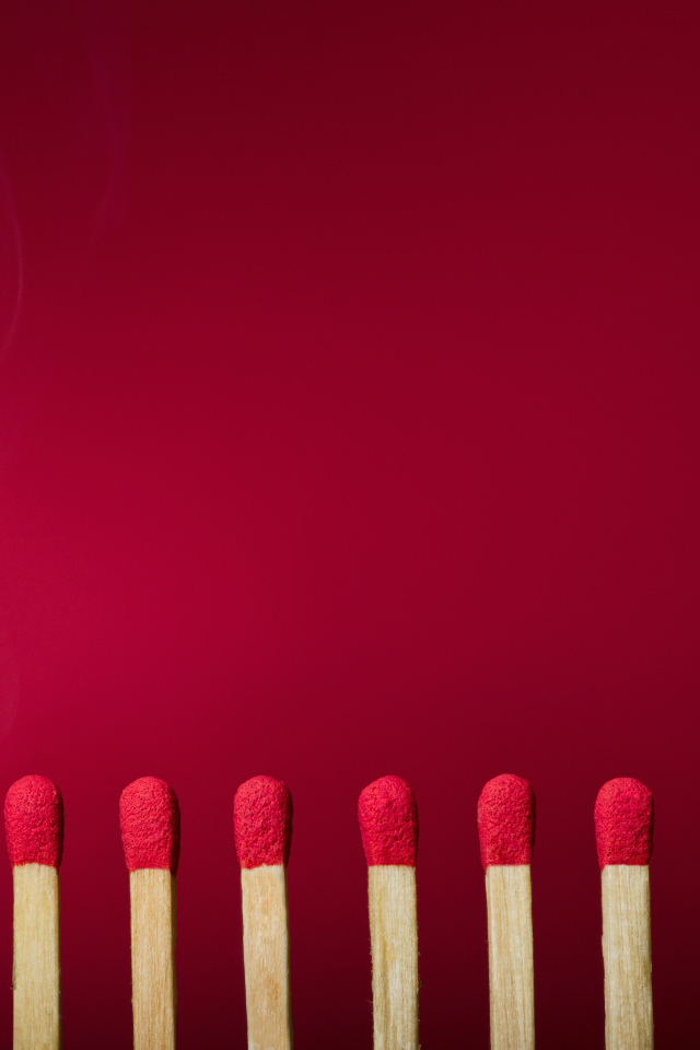 Зажженная спичка и спички на красном фоне