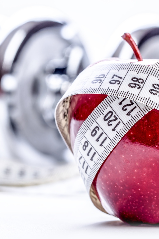 Красное яблоко перемотано мерной лентой и гантели на белом фоне