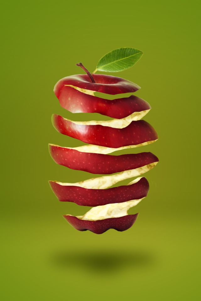 Нарезанное спиралью красное яблоко на зеленом фоне 