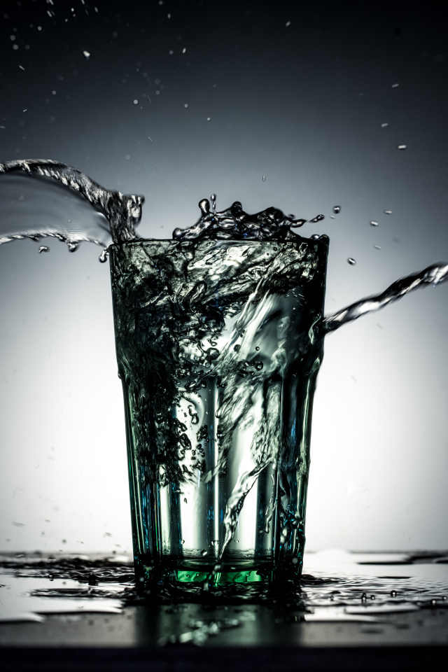 Брызги воды из стакана с водой на сером фоне