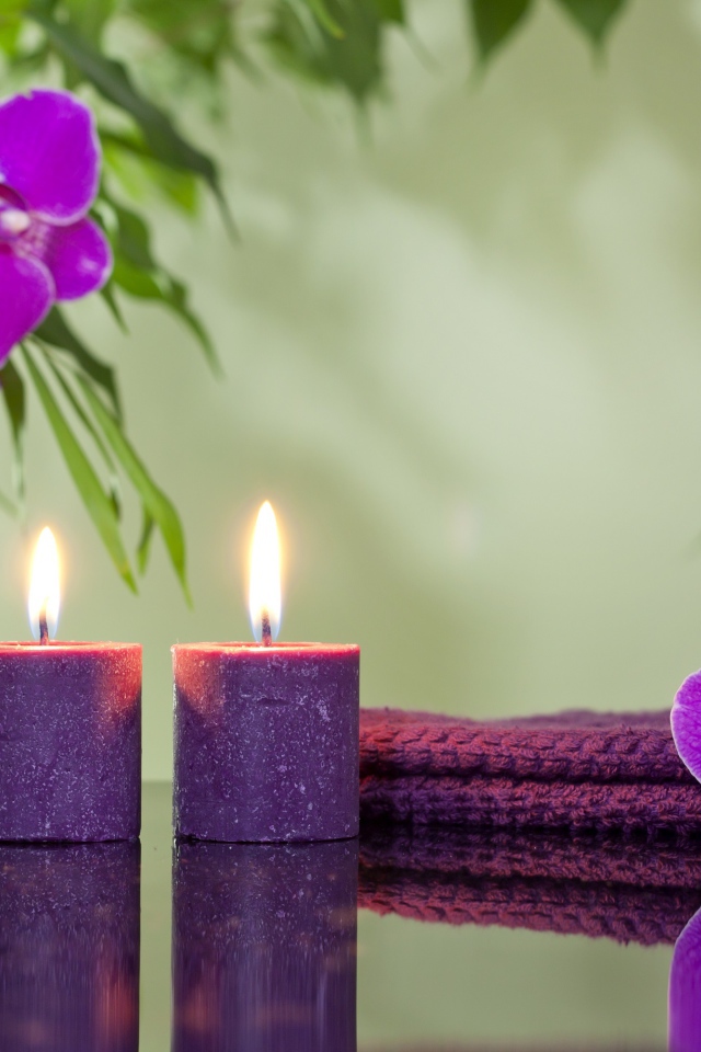 Две горящие свечи с камнями и цветами орхидеи отражаются в зеркальной поверхности стола