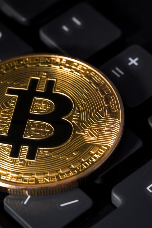 Монета биткоин лежит на черной клавиатуре