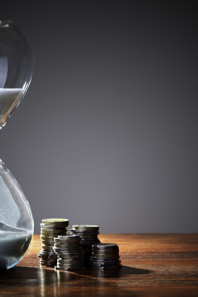 Монеты и песочные часы на столе