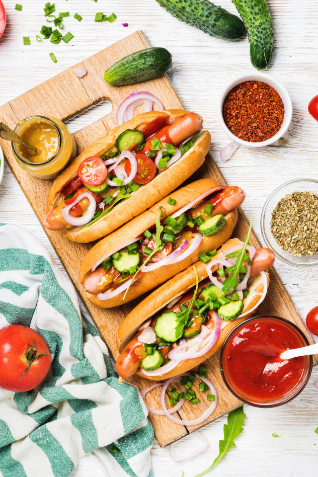 Аппетитные хотдоги на разделочной доске с овощами
