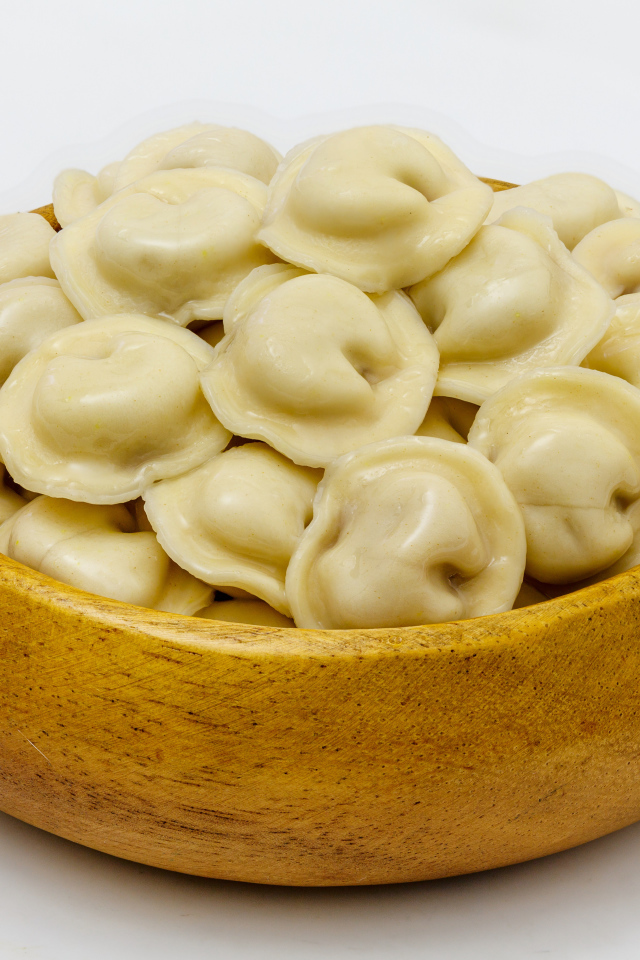 Аппетитные пельмени в деревянной миске на сером фоне