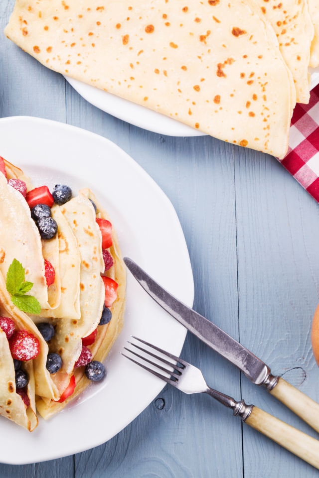 Аппетитные блинчики с ягодами на белой тарелке 