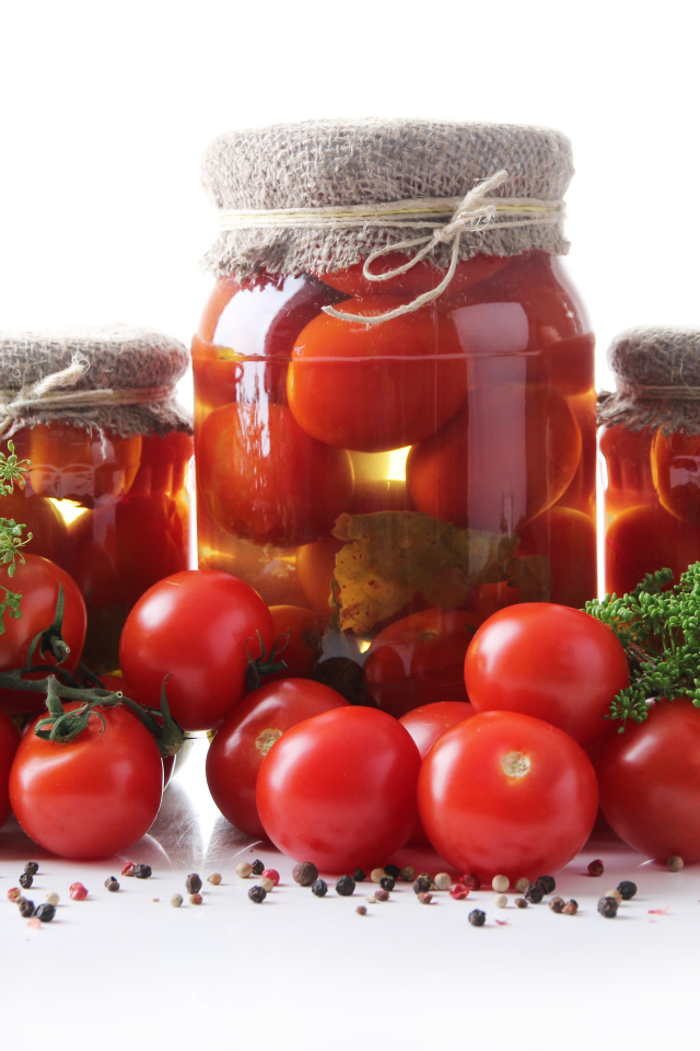 Банки с консервированными и свежими помидорами на столе со специями на белом фоне