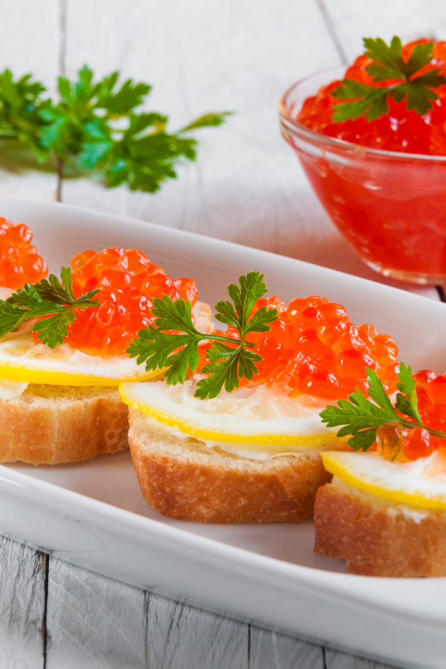 Бутырброды с красной икрой и лимонами на белой тарелке