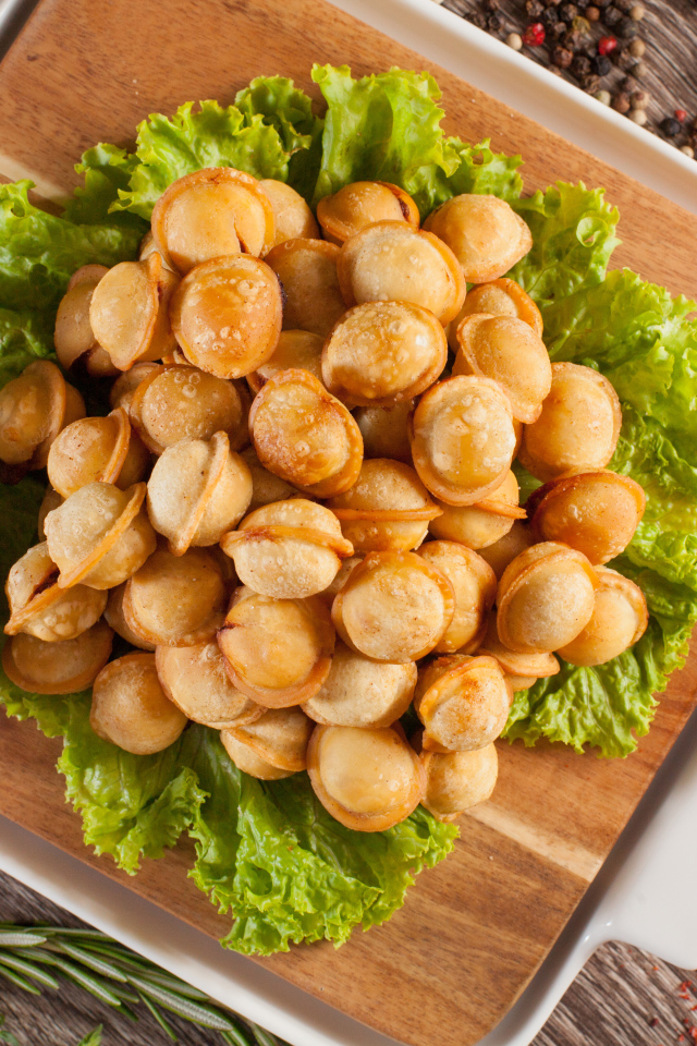 Пельмени с соусом и листьями салата лежат на разделочной доске