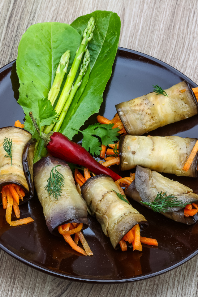 Рулетики из баклажанов с морковью на тарелке с листьями салата