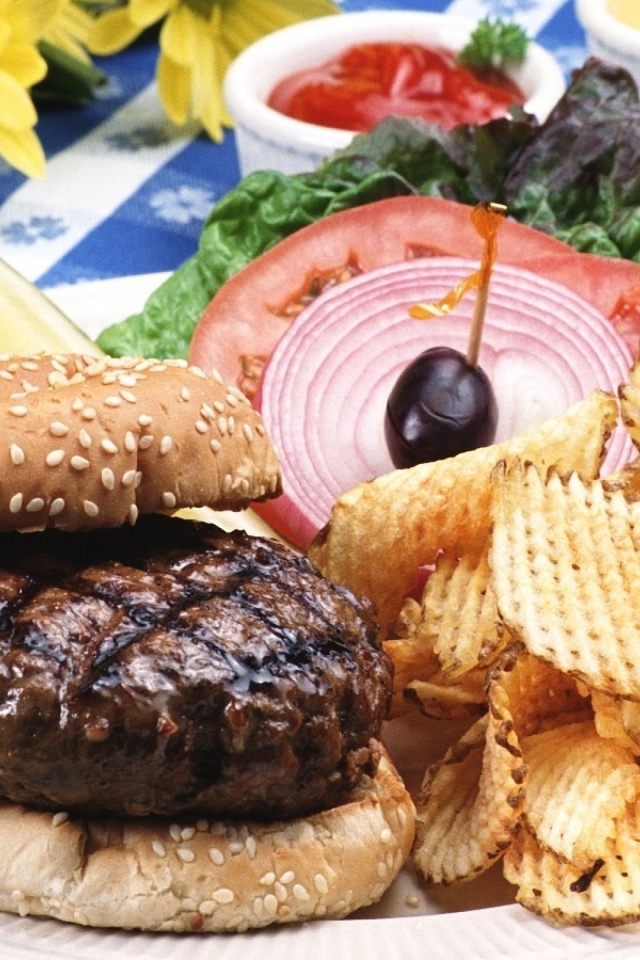 Гамбургер с котлетой и картофельные чипсы на тарелке с овощами