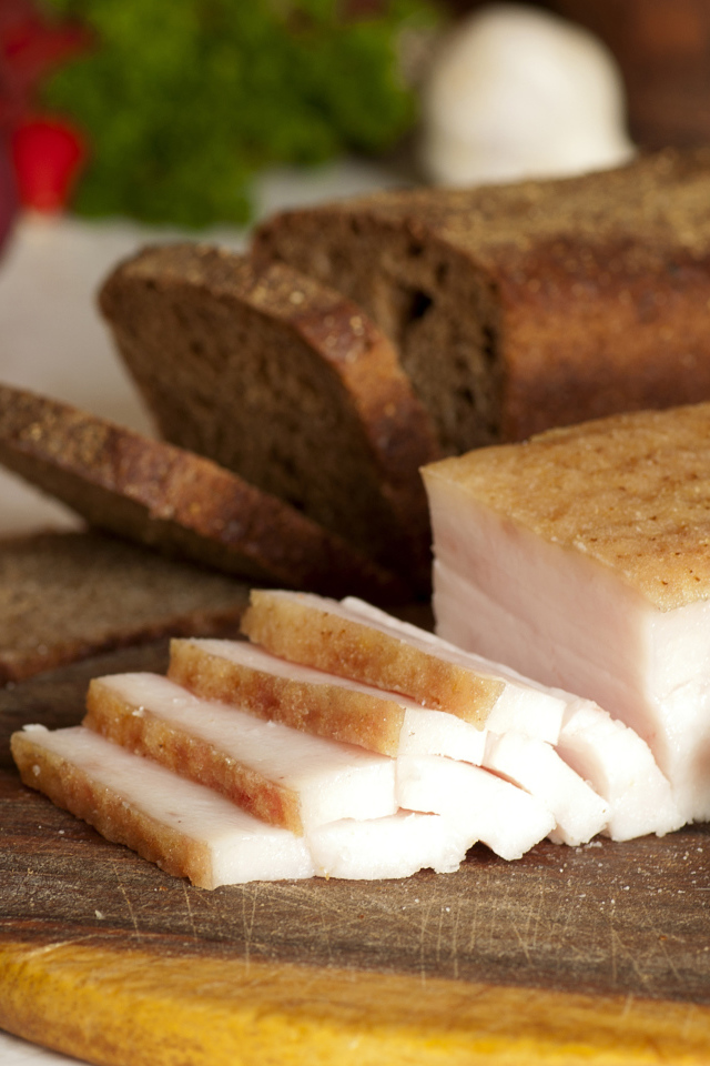 Нарезанное кусочками сало и черный хлеб на разделочной доске