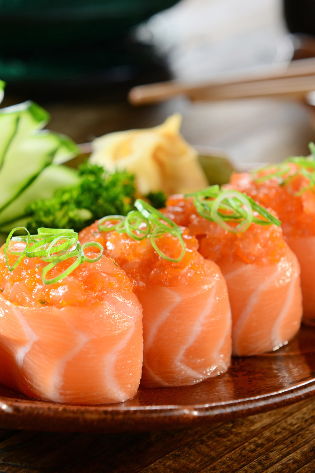 Суши из красной рыбы на тарелке со свежими огурцами и зеленью