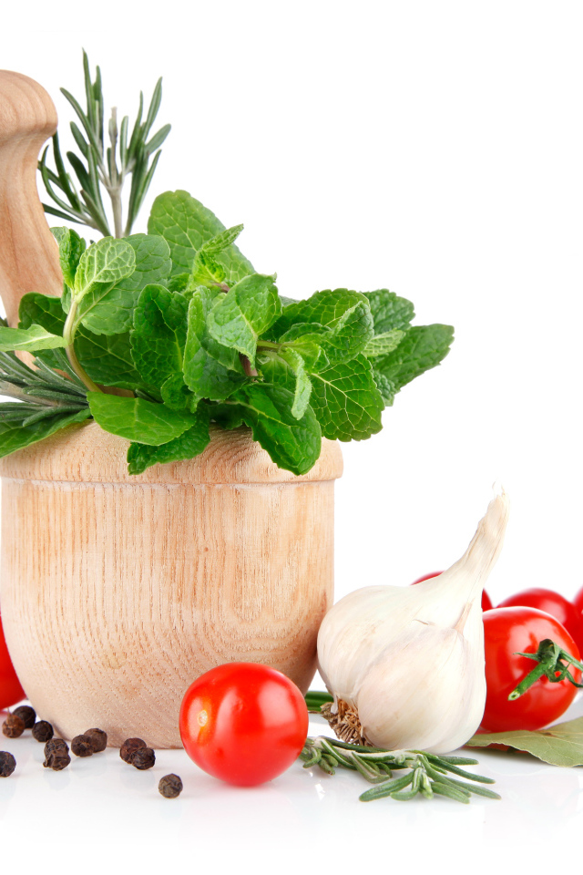 Деревянная ступа и пестик со специями и зеленью на столе с чесноком и помидорами