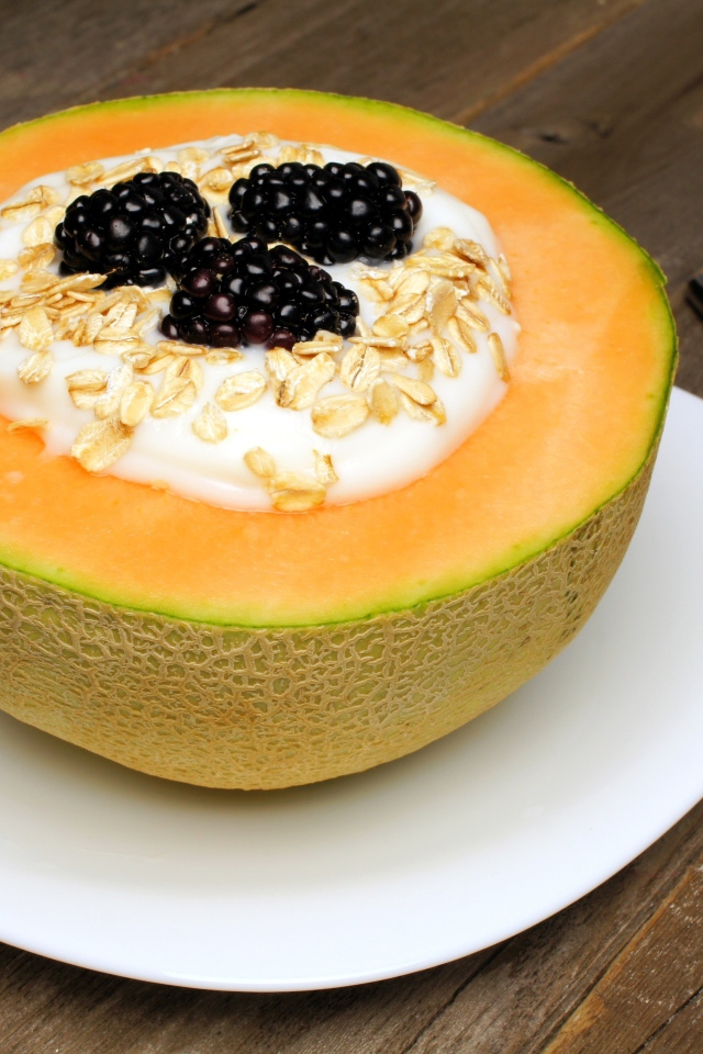 Йогурт с ежевикой и овсянкой в тарелке из свежей дыни на завтрак
