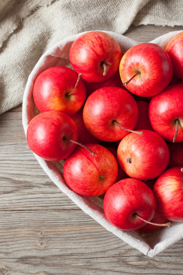 Красивые красные яблоки в тарелке в форме сердца на столе