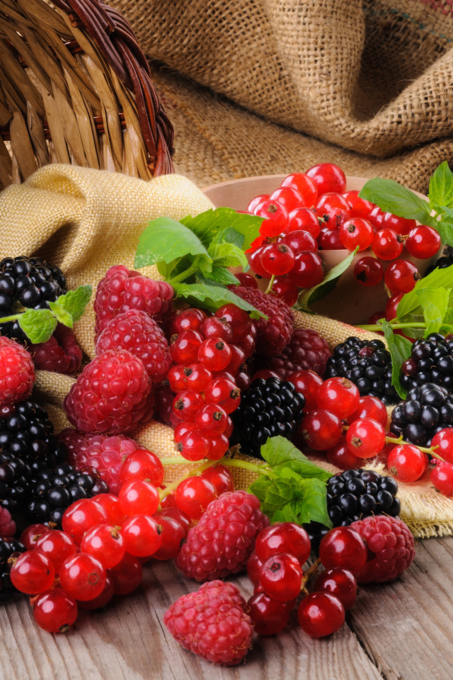 Свежие ягоды ежевики, малины и красной смородины с корзиной на столе