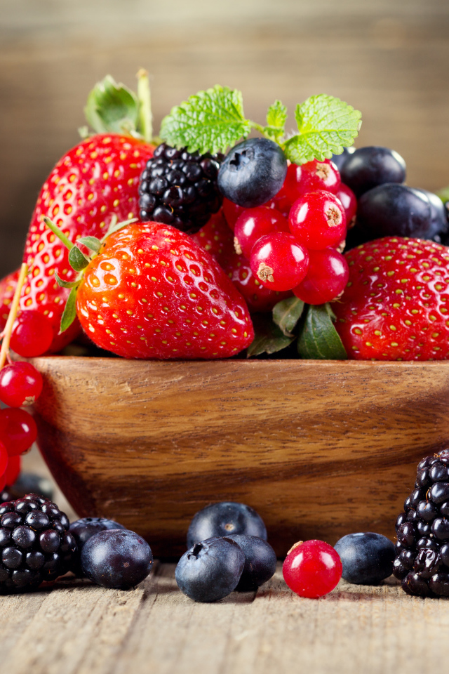 Свежие ягоды смородины, черники и клубники в деревянной тарелке на столе