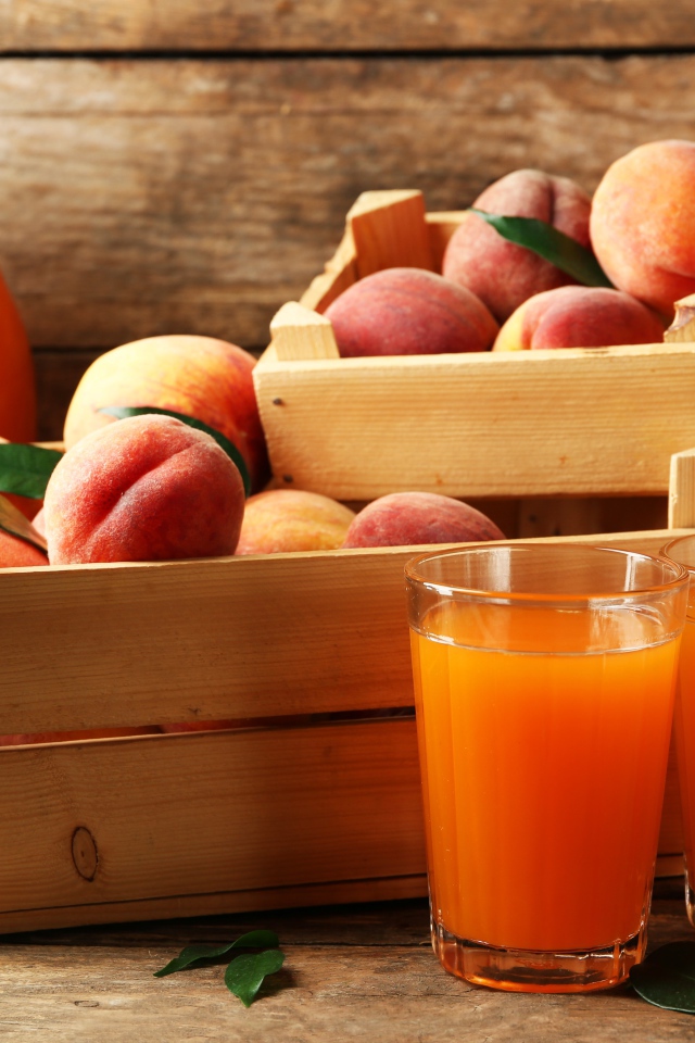 Свежие персики в деревянном ящике со свежим соком на столе