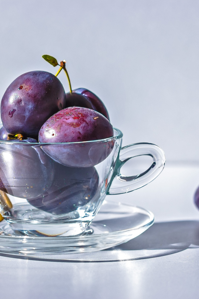 Спелые синие сливы на столе в стеклянной чашке