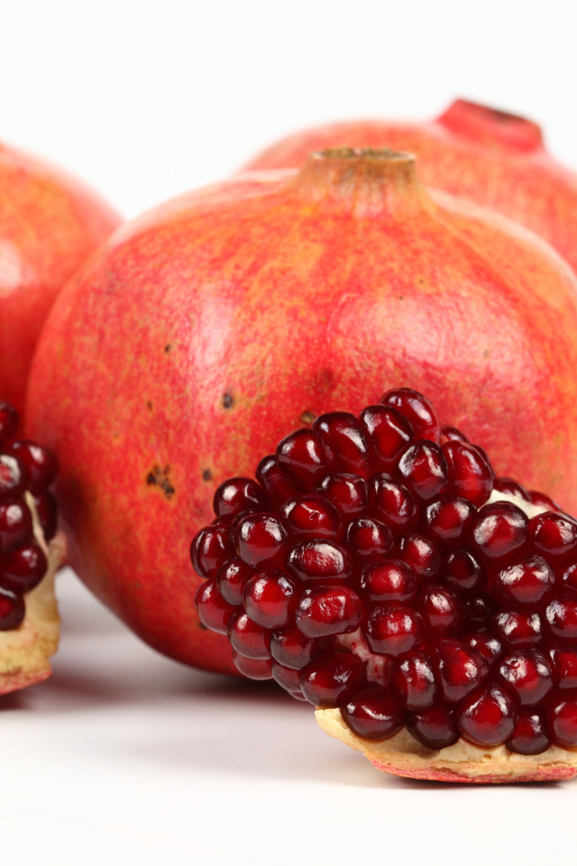 Три красных граната с ломтиками на белом фоне