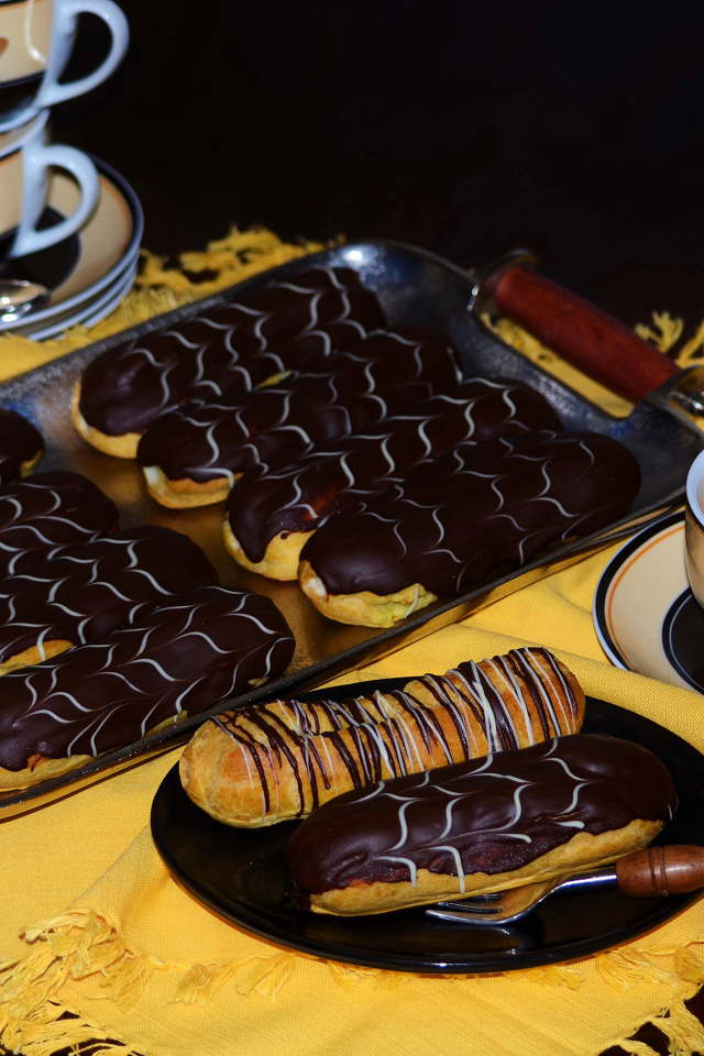 Аппетитные сладкие эклеры с шоколадом и чашками кофе на столе