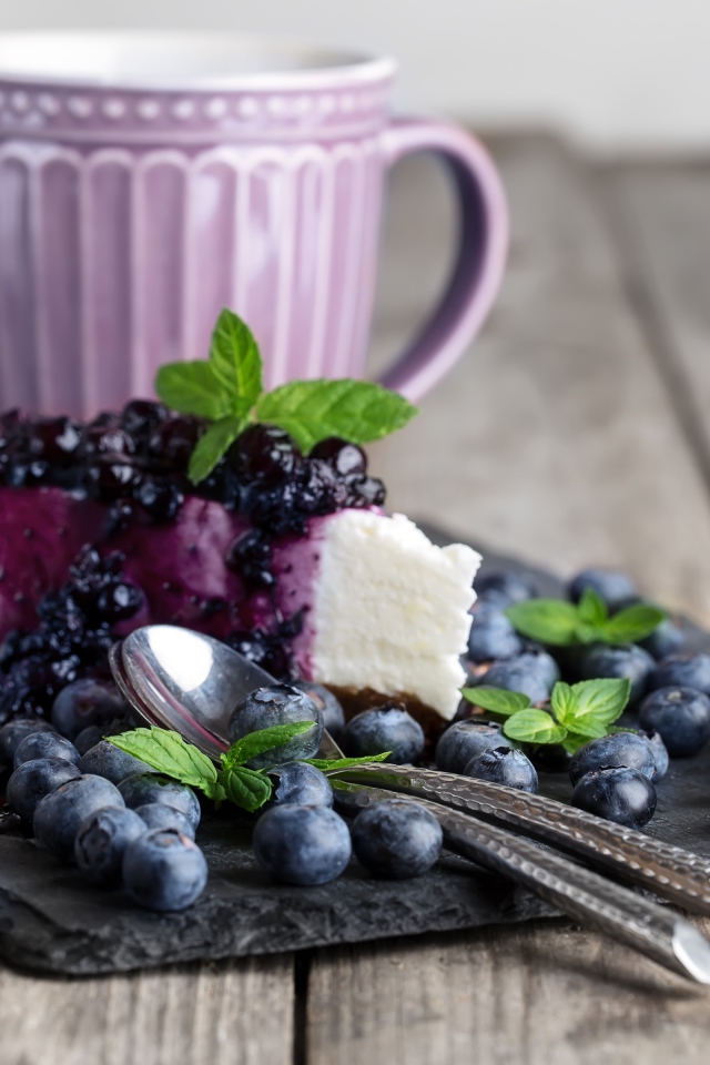 Черничный чизкейк со свежими ягодами лежит на столе с чашкой