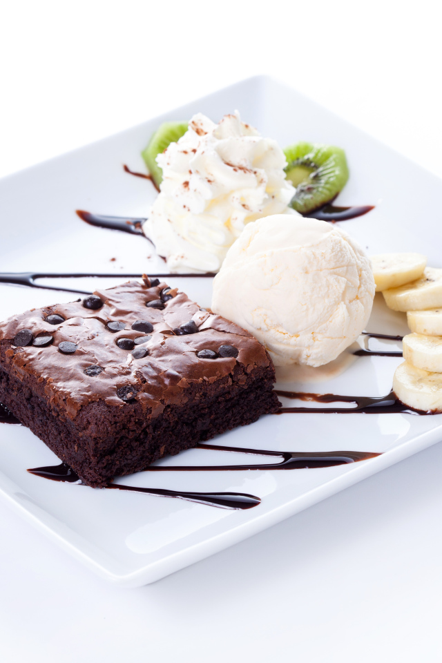 Шоколадное пирожное с мороженым, сливками и кусочками банана на белой тарелке