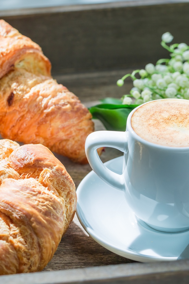 Свежие круассаны с чашкой кофе и букетом ландышей на столе