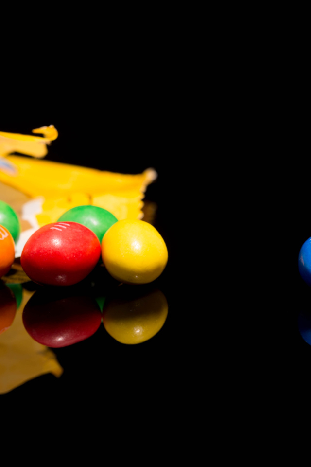 Разноцветные конфеты  M&m's отражаются в черной поверхности стола 