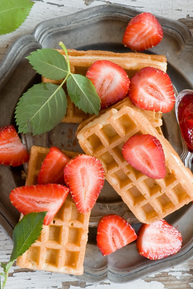 Сладкие вафли со свежей клубникой и красными розами на столе