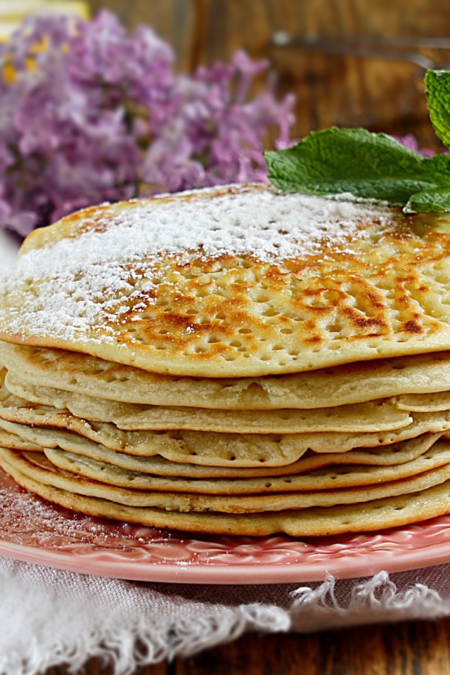 Тонкие блинчики на тарелке с сахарной пудрой и веточкой мяты