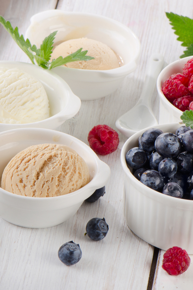 Три шарика мороженого и свежие ягоды малины и черники в белых тарелках
