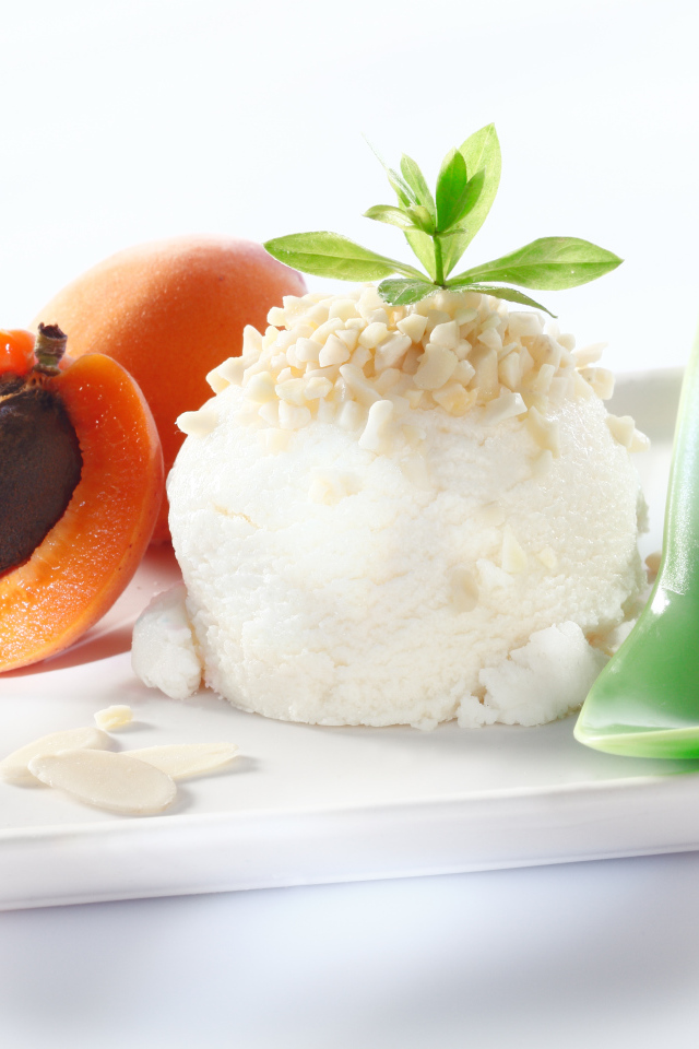 Шарик ванильного мороженого с абрикосами на белой тарелке с ложкой