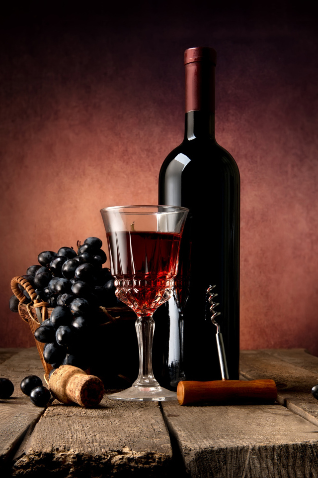 Бутылка красного вина на столе с бокалом и синим виноградом